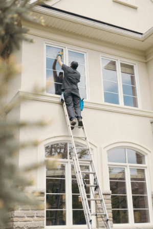 Technician on a ladder washing the upper windows of a house
