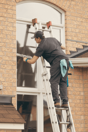 Technician on a ladder cleaning an arched second-storey window