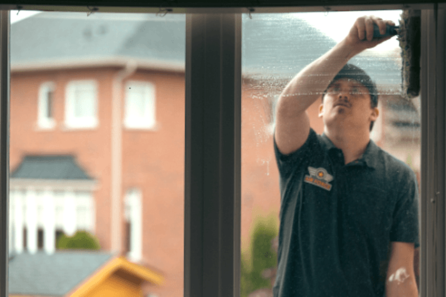 Technician washing a window from inside a home