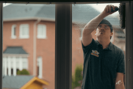 Technician scrubbing a window from inside a home