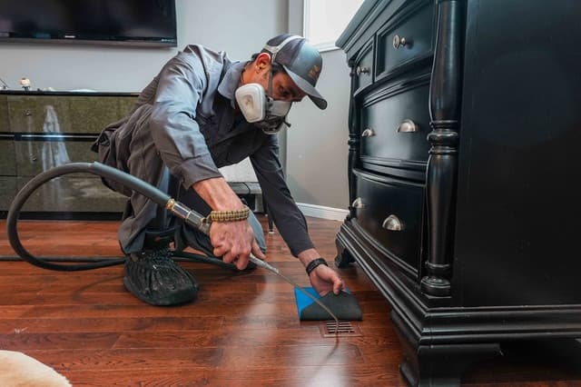 Technician cleaning a floor vent beside a dresser