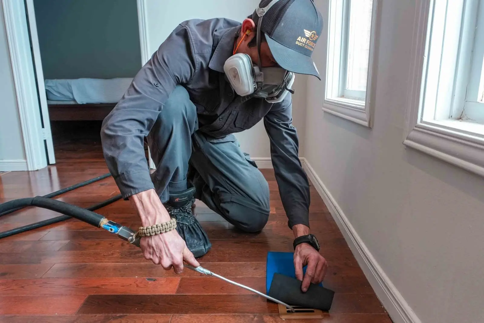 Technician cleaning a floor vent with a compressed-air tool
