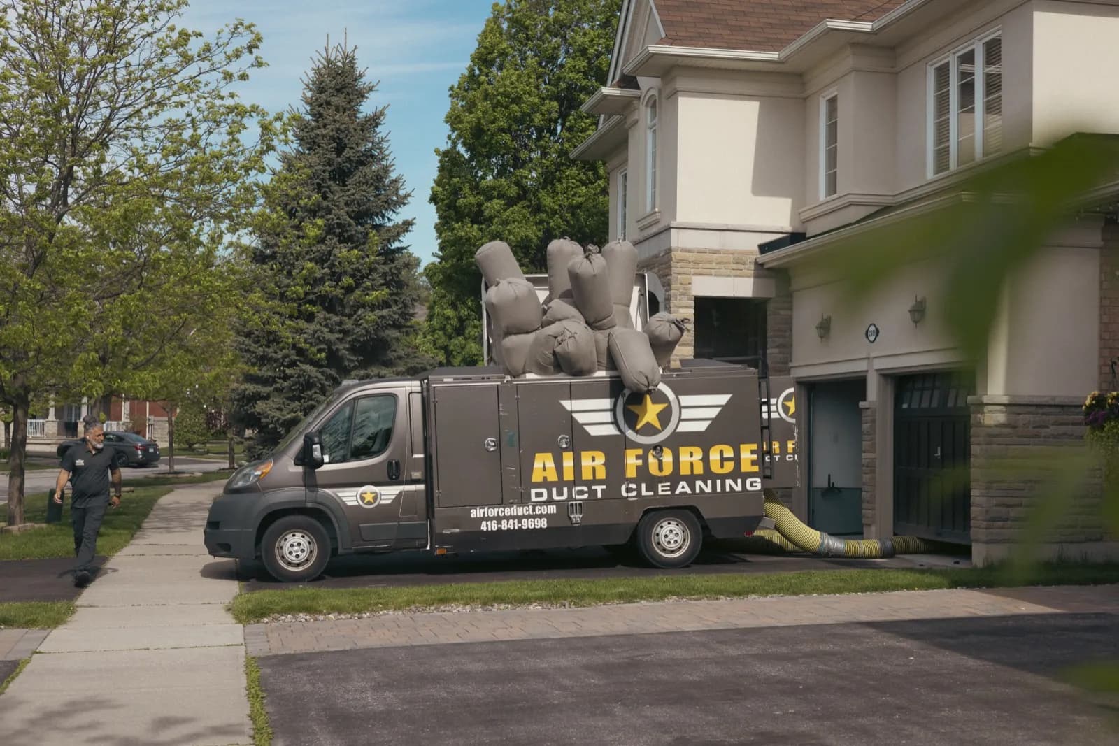 Our duct cleaning truck in a client's driveway, its vacuum hose run into the house, as a technician walks back to it