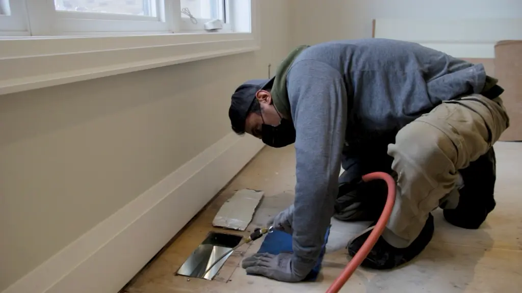 Technician cleaning a floor register with an air hose